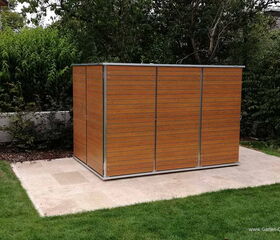 . This image shows a wooden garden shed with a modern design. The shed is placed on a concrete slab and is surrounded by a garden area with grass and trees in the background. The wood panels have horizontal lines and the structure is bordered with metal frames.