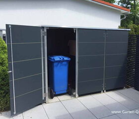 . The image shows an outdoor storage unit or shed with open doors. Inside, there is a blue wheeled trash bin. The storage unit is located on a patio or tiled surface, next to some greenery.