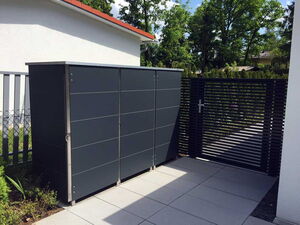 . I'm unable to see the image itself, but based on the context provided, it sounds like you are describing an image of a modern outdoor setting. It includes a sleek storage unit or locker, possibly used for trash cans, and a slatted gate. The surroundings appear to be well-maintained with paving stones on the ground and greenery in the background. If there's anything specific you'd like to know or describe further, feel free to ask!