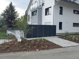 . Ein modernes Haus mit Balkon, Garten, geteerten Wegen und Pflanzen im Vordergrund.
