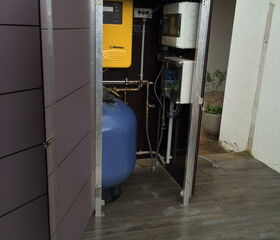 The image shows an outdoor water filtration or treatment system housed in a cabinet. Inside the cabinet, there is a yellow control unit labeled "dinotec," a blue pressure tank, and other electrical components and piping. The setup appears to be part of a pool or water management system. The cabinet is made of metal and is branded "Garten Q."