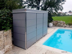 . Ein graues Gartenhäuschen steht neben einem Pool, umgeben von Steinmauern und einem grünen Rasen.