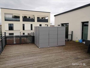 Dachterrasse mit Holzboden, modernem Gebäude, grauem Schrank, Pflanzenkübeln und Gießkannen.