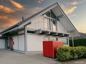 . Modernes Haus mit Satteldach, Balkon, rotem Schrank und grünen Büschen bei Sonnenuntergang.