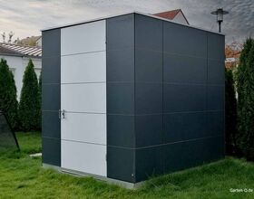 Ein moderner, dunkler Gartenschuppen aus Metall mit weißen Akzenten, umgeben von Rasen und Bäumen.