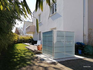 . Ein moderner Garten mit Terrasse, Pflanzen und einem kleinen, grauen Schuppen.