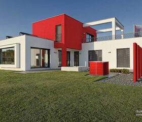 . Modernes Gebäude mit weiß-roter Fassade, großen Fenstern und gepflegtem Rasen im Vordergrund.