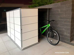 . Ein Fahrrad steht teils in einem modernen, weißen Schuppen mit Steinwandhintergrund.