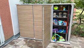 . Ein Gartenschrank mit geöffnetem Fach, gefüllt mit Gartenwerkzeugen, Spielzeug und verschiedenen Haushaltsgegenständen.