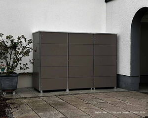 Ein graues Outdoor-Möbelstück an einer weißen Wand neben einem Pflanzenkübel mit Strauch.