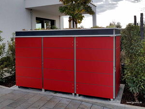 . Roter Gartenschrank neben einem Haus, umgeben von Pflanzen und Pflastersteinen.