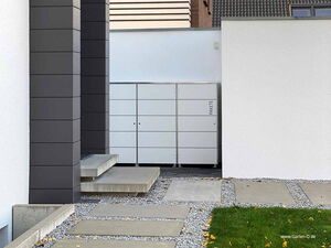 . Moderne weiße Paketboxen neben Stufen in einem minimalistischen Garten mit Kiesweg und Betonplatten.