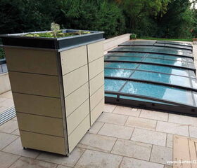 . Ein Gartenaufbewahrungsschrank mit bepflanztem Dach und ein überdachter Pool im Hintergrund.