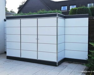. Ein moderner Gartenschrank aus weißen Lamellen mit schwarzem Rahmen ist auf einer Terrasse neben einem Haus platziert.
