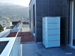 . Ein moderner Balkon mit einem weißen Schrank, Gebäuden im Hintergrund und Bergen in der Ferne.