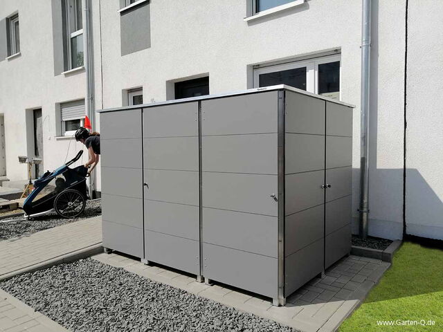Ein Schuppen vor einem Wohnhaus mit einer Person, die einen Kinderanhänger schiebt.