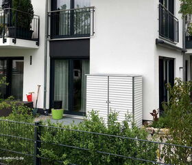 Ein moderner Garten mit Balkon, weißem Schrank, Pflanzendekor und Zaun vor einem Gebäude.