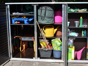 . Ein geöffneter Gartenschrank mit Gießkannen, Werkzeugen, Eimern, Dünger und anderem Gartenbedarf.