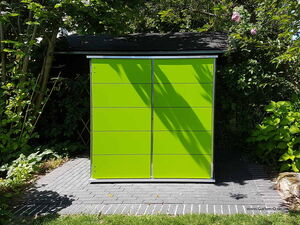 . The image shows a garden storage unit with a bright green color. It has a modern, minimalist design with a sleek, rectangular shape and paneling. The unit is situated on a paved area with greenery and trees surrounding it.