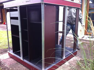 . Ein offener Gartenschrank mit Regalen, daneben eine Person in einer Jacke.