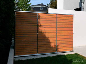 . This image shows a storage unit or shed with a modern design featuring horizontal wooden slats and metallic framing. It is set outdoors, with some grass in the foreground. There's also a house and some trees visible in the background. The unit appears to be a part of a garden setup, as indicated by the branding.