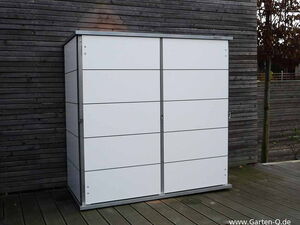 . Ein weißer Gartenschrank vor einer Holzpaneelwand im Freien.