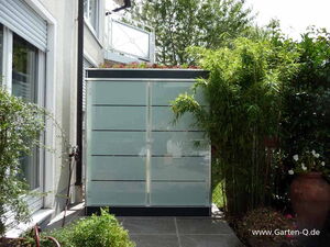 . Moderne Gartenschrank vor einem Haus, umgeben von Pflanzen und einer Terrasse.