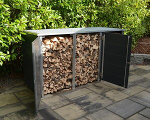 The image shows a storage area for firewood. It is an outdoor wooden log holder, with doors that are open, revealing a neatly stacked pile of firewood inside. The storage is situated on a patio with stone tiles and is backed by green foliage.