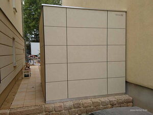 . Ein modernes Gartenhaus zwischen zwei Gebäuden, beige mit quadratischen Platten gestaltet.