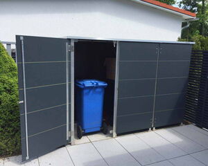 . The image shows an outdoor storage unit with two open doors. Inside, there is a blue wheeled trash bin. The unit is positioned next to a white wall and is surrounded by greenery and a paved area.