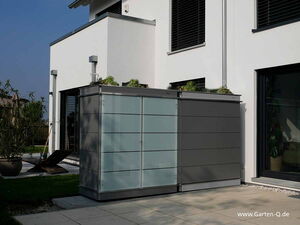 . Ein Gartenschrank steht neben einem modernen weißen Gebäude mit großen Fenstern und Pflanzen auf dem Dach.
