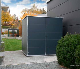 . The image shows a modern garden storage shed with a sleek design, placed on a patio area. It is situated next to a building and a neatly trimmed bush, with a grassy area and some autumn foliage in the background. The website "www.Garten-Q.de" is visible in the bottom right corner.