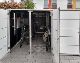 Ein geöffneter Schuppen mit zwei Fahrrädern, einer Leiter und Gartengeräten.