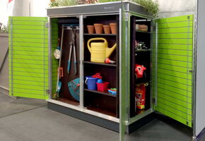 . Here's an array listing the items in the image:

```plaintext
[
  "Green outdoor storage cabinet",
  "Gardening tools (pruning shears, rake)",
  "Yellow watering can",
  "Small flower pots",
  "Red and blue plastic buckets",
  "Gardening gloves",
  "Plant fertilizer bag",
  "Plants on top of the cabinet"
]
```