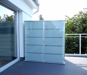 . Balkon mit Glas-Trennwand, moderne Terrasse, Pflanzen im Hintergrund.