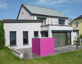 . Modernes Haus mit Rasen, Terrasse und einem pinken Container im Garten.