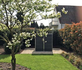 . Ein Garten mit grünem Rasen, blühendem Baum und einem modernen Solarpanel vor einem Haus.