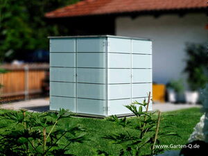 . The image features a sleek, modern storage unit situated outdoors on a lawn. The structure is cube-shaped with a minimalist design, possibly used for storing garden tools or equipment. It appears to be made of metal or a similar material, and it's set against a backdrop of a garden with some plants and a building nearby.