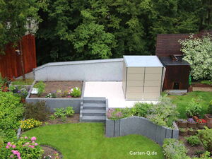 . Ein gepflegter Garten mit Blumenbeeten, Rasenfläche, Treppe und einer modernen Gartenbox auf einer Terrasse.