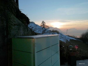 . Ein Garten mit Blick auf schneebedeckte Hügel und Sonnenuntergang. Ein großer, moderner Schrank im Vordergrund.