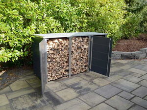 . The image shows a metal storage shed for firewood, with two doors open, revealing a stack of chopped wood inside. The shed is placed on a stone patio with greenery in the background.