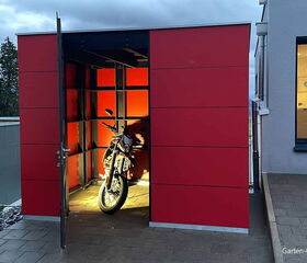 Ein roter Schuppen mit offener Tür, darin steht ein Motorrad.