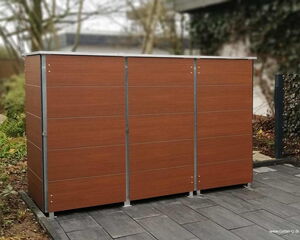 . The image shows a modern outdoor storage unit with a sleek design. It has a wood-like finish and is supported by metal frames. The unit is placed on a paved surface, presumably in a garden or backyard setting. There's vegetation and a fence visible in the background.