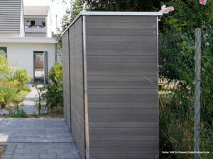 . Ein moderner Schuppen im Garten mit grauen Paneelen und Pflasterweg. Haus und bunte Blumen im Hintergrund.