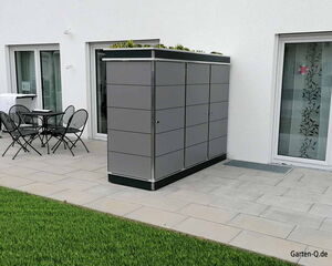 Gartenmöbelset und großer Schrank auf einer Terrasse neben einem Haus mit Rasen.
