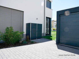 . Moderne Hausfassade mit Gartenschrank, Pflanze, Garagentor und gepflastertem Hof.
