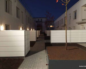 . Moderne Wohnanlage bei Nacht mit Zäunen, gepflastertem Weg, beleuchteten Gebäuden und Bäumen.