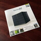 This image shows a brochure or magazine on a wooden surface. The cover features the word "Garten[Q]" and an image of a sleek, modern garden storage unit or shed. There are also smaller images and some text at the bottom, likely describing different features or models.