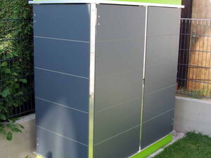 . The image shows a modern-looking outdoor storage unit. It has a sleek design with dark gray panels and bright green accents at the top and bottom. The top seems to have a small planter section with plants growing in it. It's set on a lawn near a fence and some foliage.