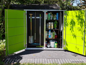 . In the image, there is an outdoor storage cabinet with open doors. Inside, you can see:

1. **Gardening tools**: 
   - A shovel
   - A broom
   - A digging fork

2. **Shelves containing**:
   - Various gardening products and supplies
   - Bags and containers likely holding seeds, fertilizers, or soil additives
   - A watering can

The cabinet is placed outdoors on a stone surface with surrounding plants and trees.